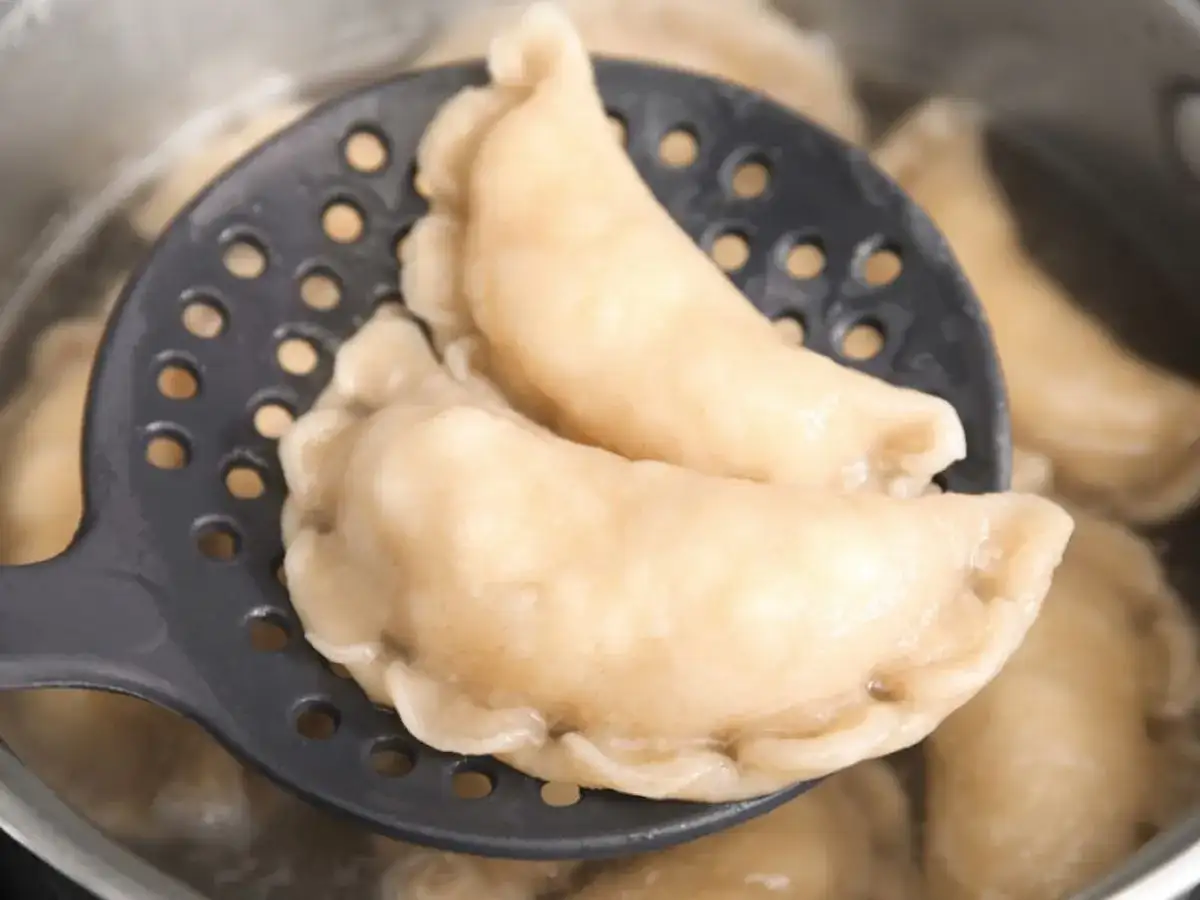 Gotowe pierogi z serem na łyżce cedzakowej, gotujące się w garnku. Idealne, by pokazać, jak zrobić pierogi z serem.