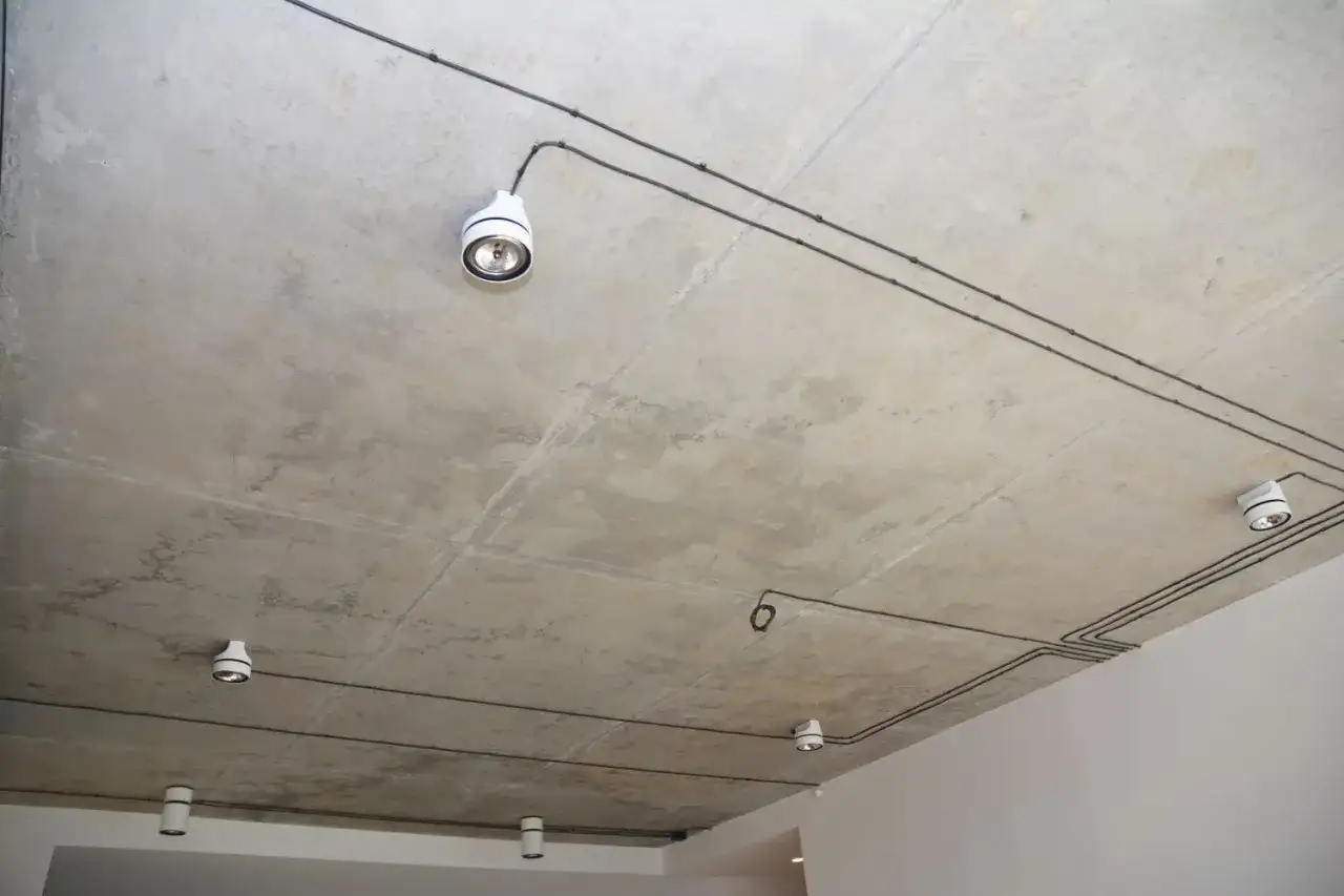 Nowoczesna instalacja elektryczna natynkowa na betonowym suficie z kilkoma białymi oprawami oświetleniowymi.