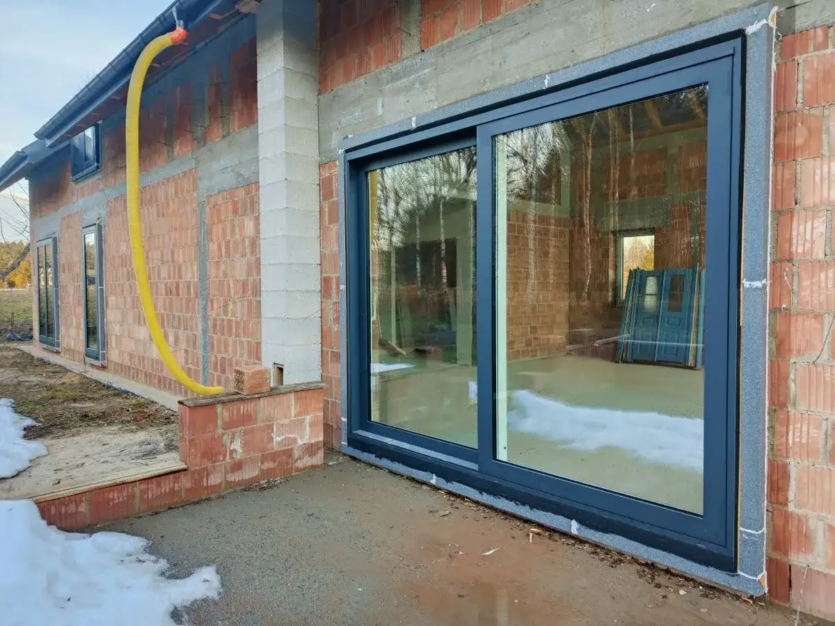 Nowe okna przesuwne w trakcie ciepłego montażu. Widać izolację i przygotowanie do wykończenia.