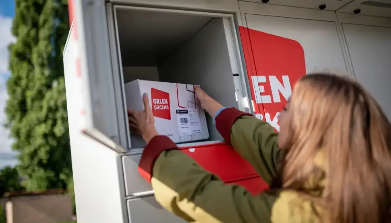 Kobieta wkłada paczkę z logo "Orlen paczka" do skrytki automatu paczkowego.