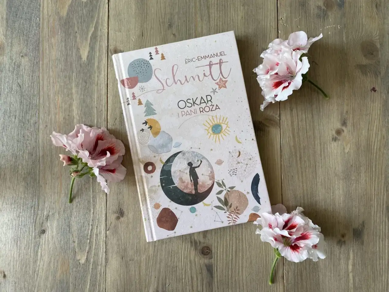 Recenzja książki "Oskar i Pani Róża" na tle drewnianych desek, ozdobiona delikatnymi kwiatami.