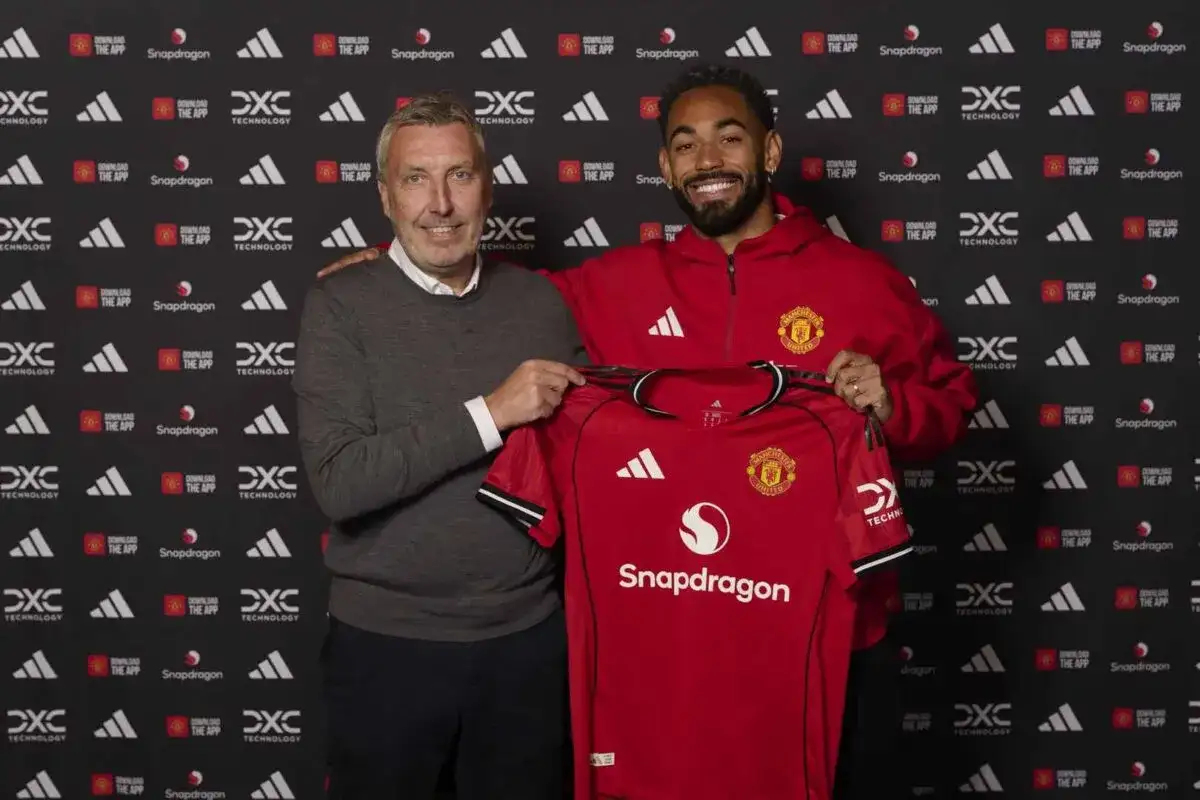 Dwóch mężczyzn prezentuje nowy strój Manchester United. Jeden z nich, ubrany w szary sweter, trzyma koszulkę, a drugi, w czerwonej bluzie, uśmiecha się. To część prezentacji manchester united skład.