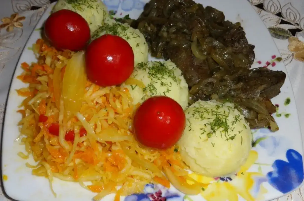 Talerz z wątróbką drobiową, ziemniakami, surówką z kapusty i marchewki oraz pomidorkami koktajlowymi.