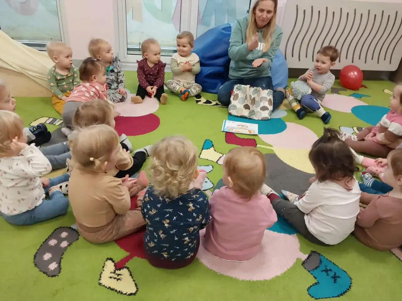 Nauczycielka pokazuje dzieciom w żłobku obrazki, inspirując angielski w żłobku pomysły. Dzieci siedzą na kolorowym dywanie.