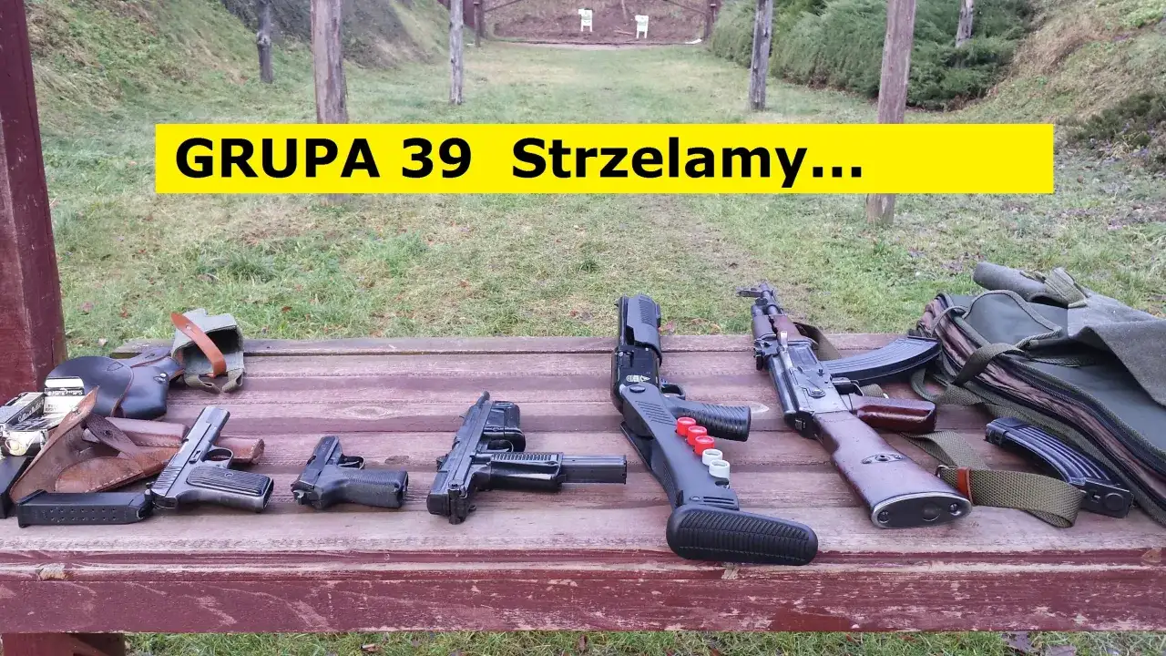 Na drewnianym stole leżą różne rodzaje broni palnej, w tle strzelnica.