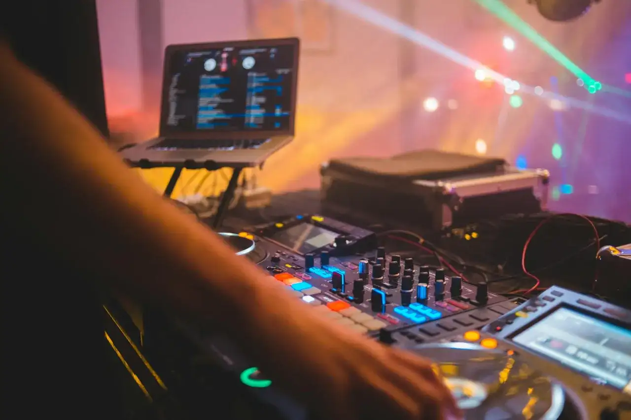 DJ przy konsoli tworzy utwór muzyczny w wolnym tempie, oświetlony kolorowymi światłami dyskotekowymi.