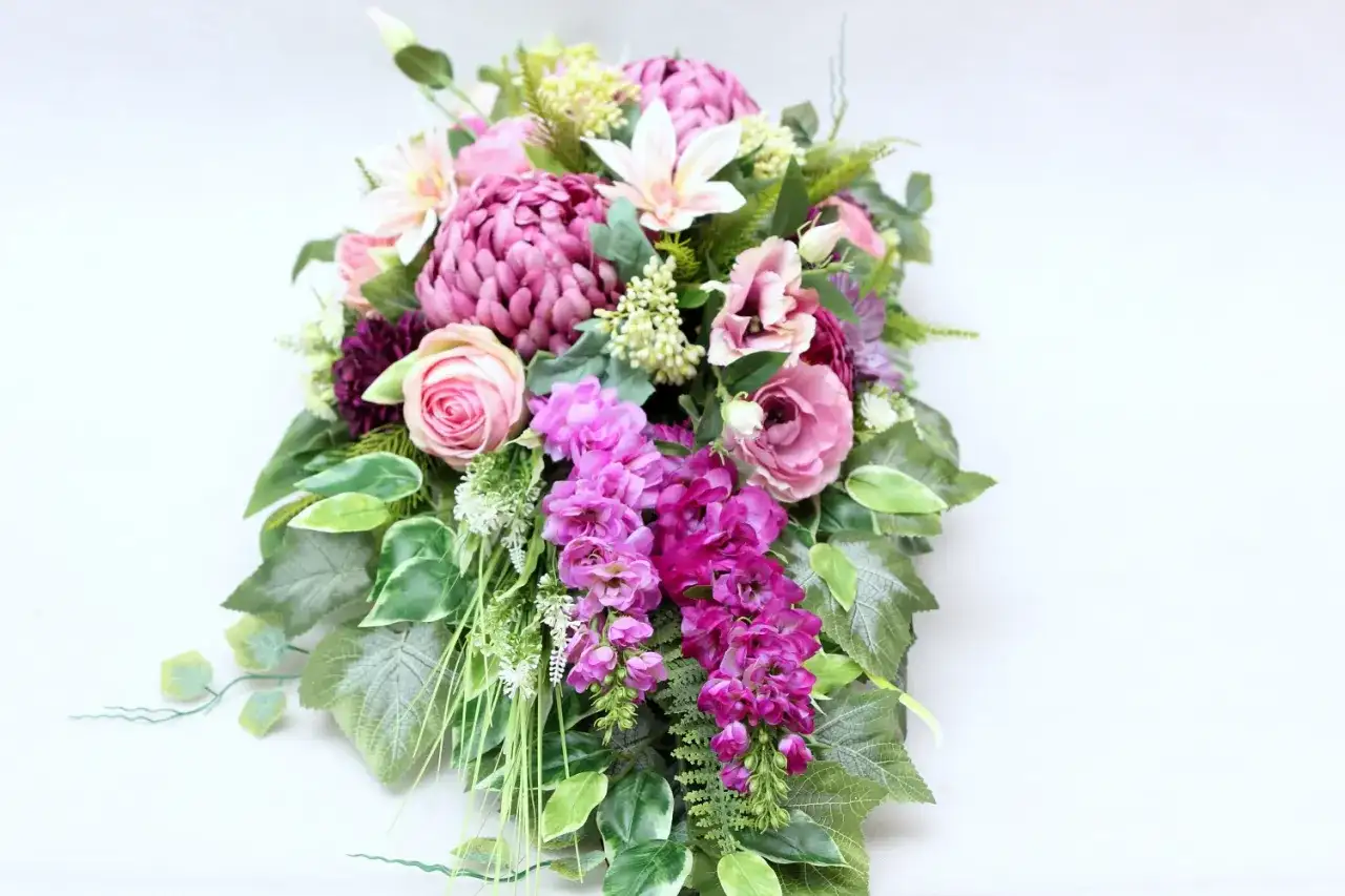 Wiązanka pogrzebowa z różowych i fioletowych kwiatów z zielonymi liśćmi.