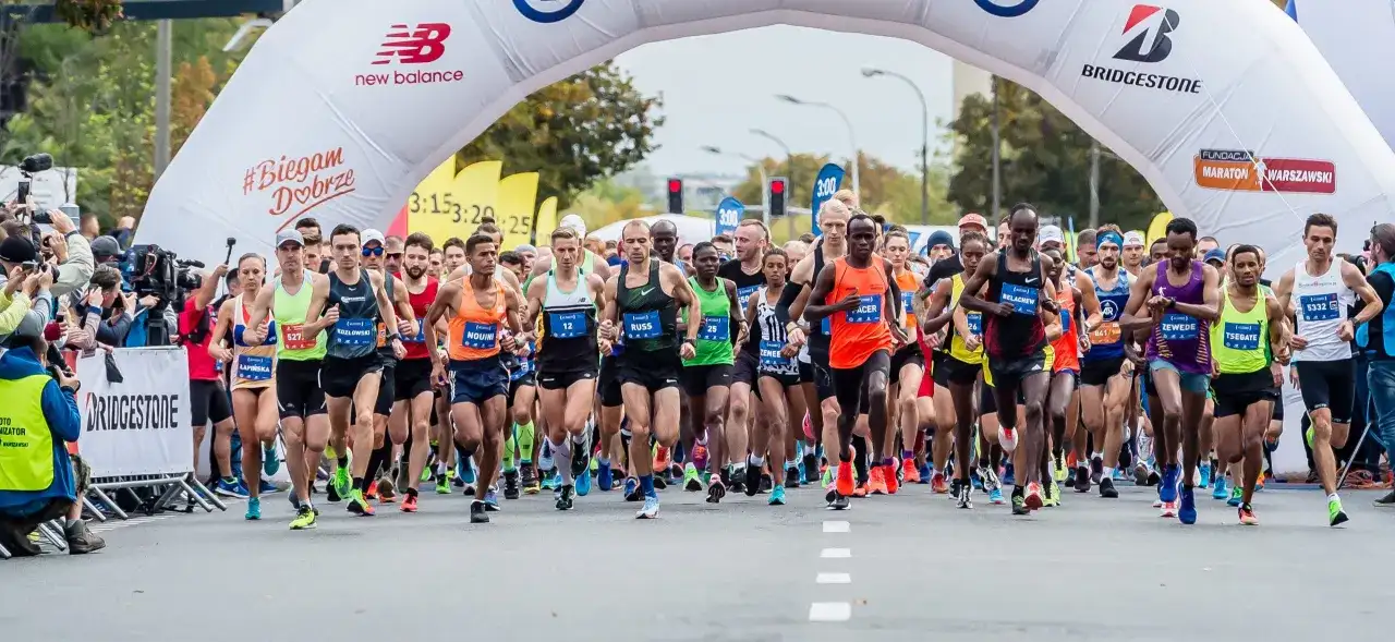 Start maratonu dla amatora. Zawodnicy pod łukiem startowym, tłum kibiców i kamerzystów.