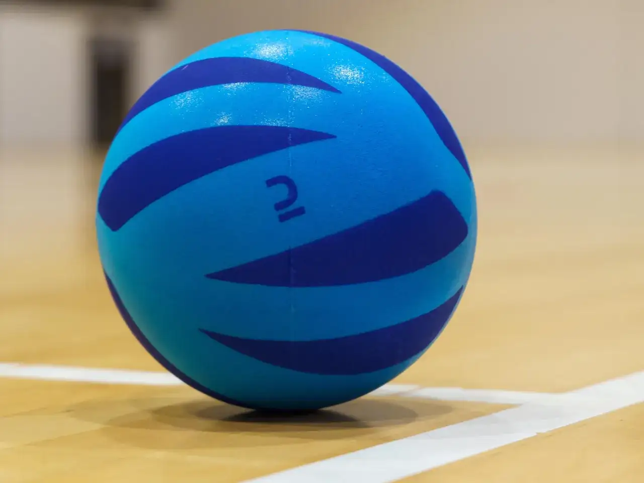 Niebieska piłka do pilatesu z ciemniejszymi pasami na drewnianej podłodze.