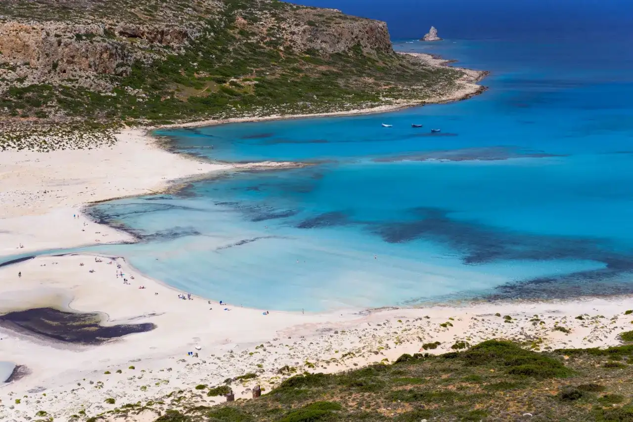 Widok na turkusową zatokę z piaszczystą plażą i skalistym wybrzeżem.