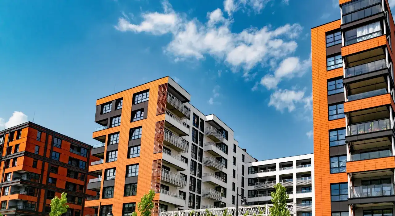 Nowoczesne bloki mieszkalne z pomarańczowymi i białymi elewacjami. Czy deweloper może zmienić cenę mieszkania? To pytanie nurtuje kupujących.
