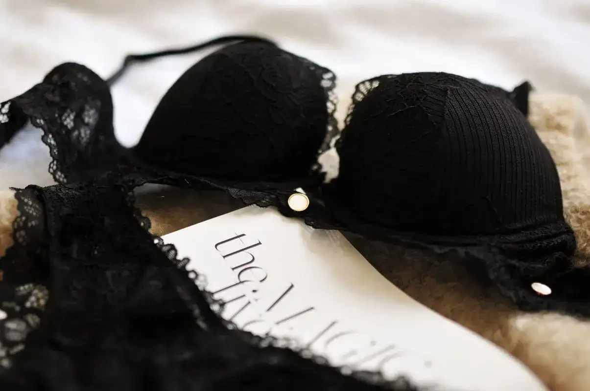 Czarny biustonosz z koronką leży na miękkim materiale obok białej karty z napisem "the Magic".