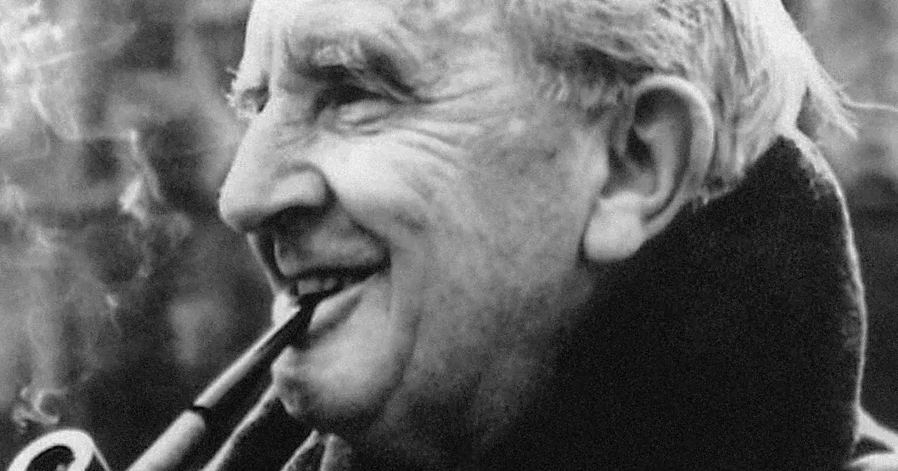 J.R.R. Tolkien, autor książki Hobbit, pali fajkę, uśmiechając się.