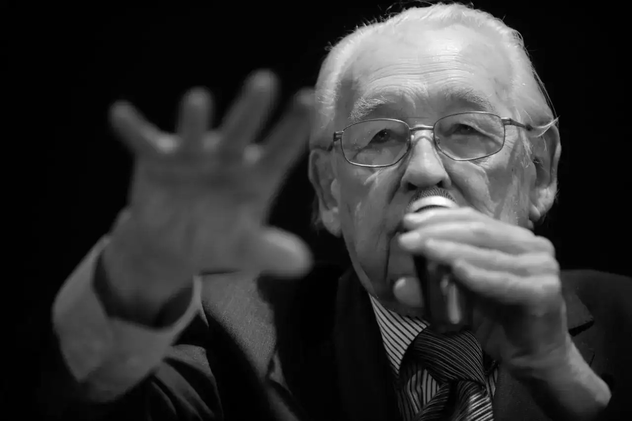 Portret starszego mężczyzny w okularach, trzymającego mikrofon. Wśród znanych reżyserów polskich, jego postać budzi szacunek.
