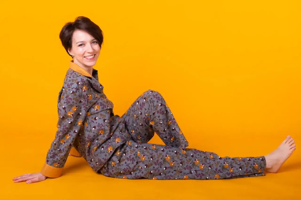 Kobieta w szarej piżamie w liski i kwiaty siedzi na żółtym tle.