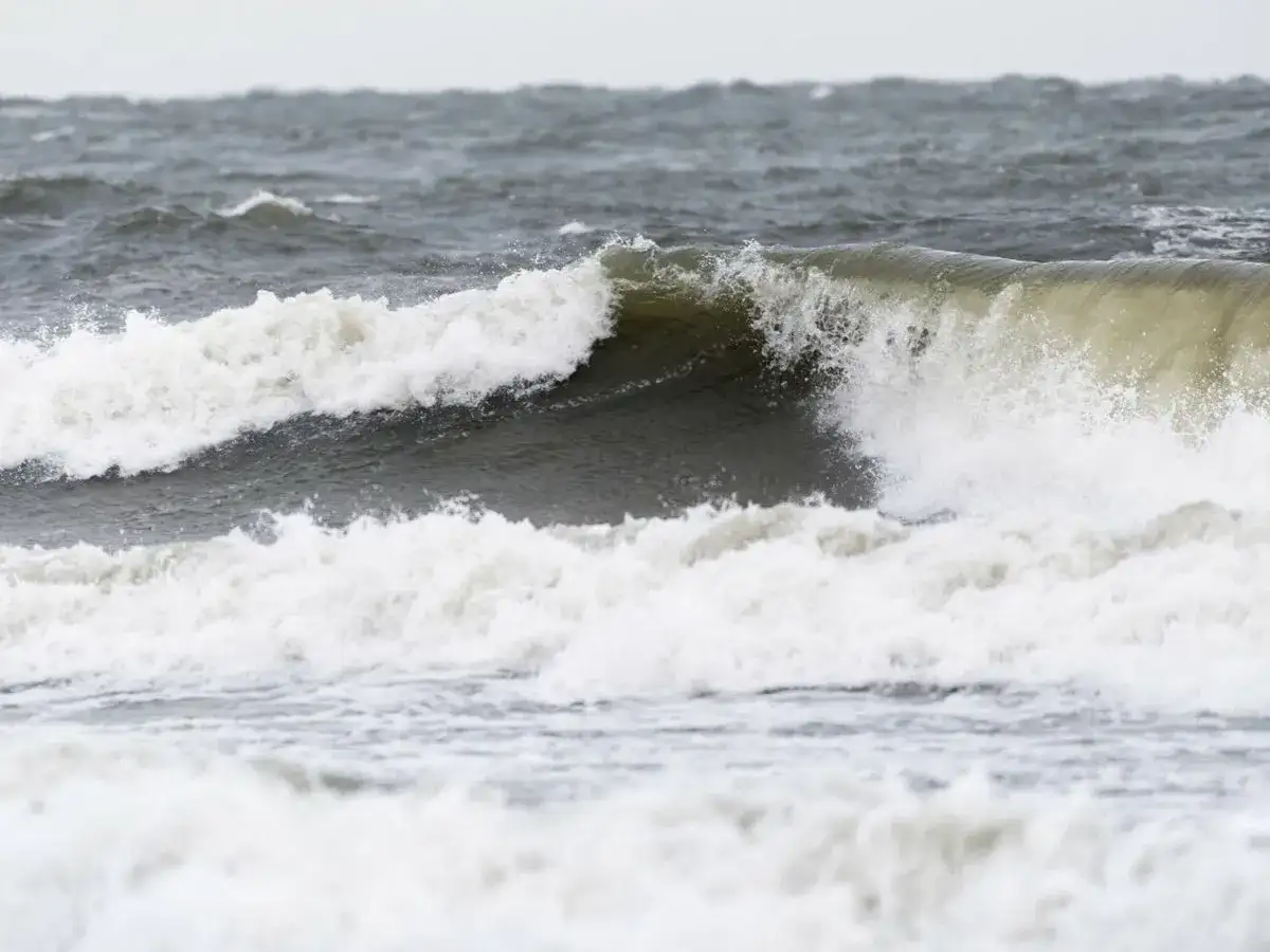 Potężne fale rozbijają się o brzeg, pokazując siłę, kiedy są sztormy na Bałtyku. Woda jest wzburzona i szara.