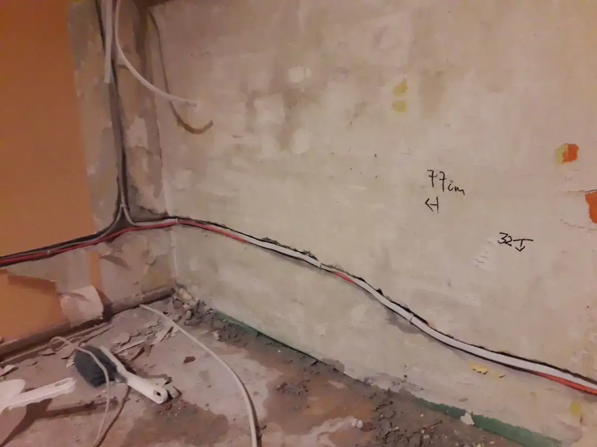 Skrętka obok kabla elektrycznego biegnie wzdłuż ściany. Na tynku widoczne oznaczenia "77cm" i "32J".