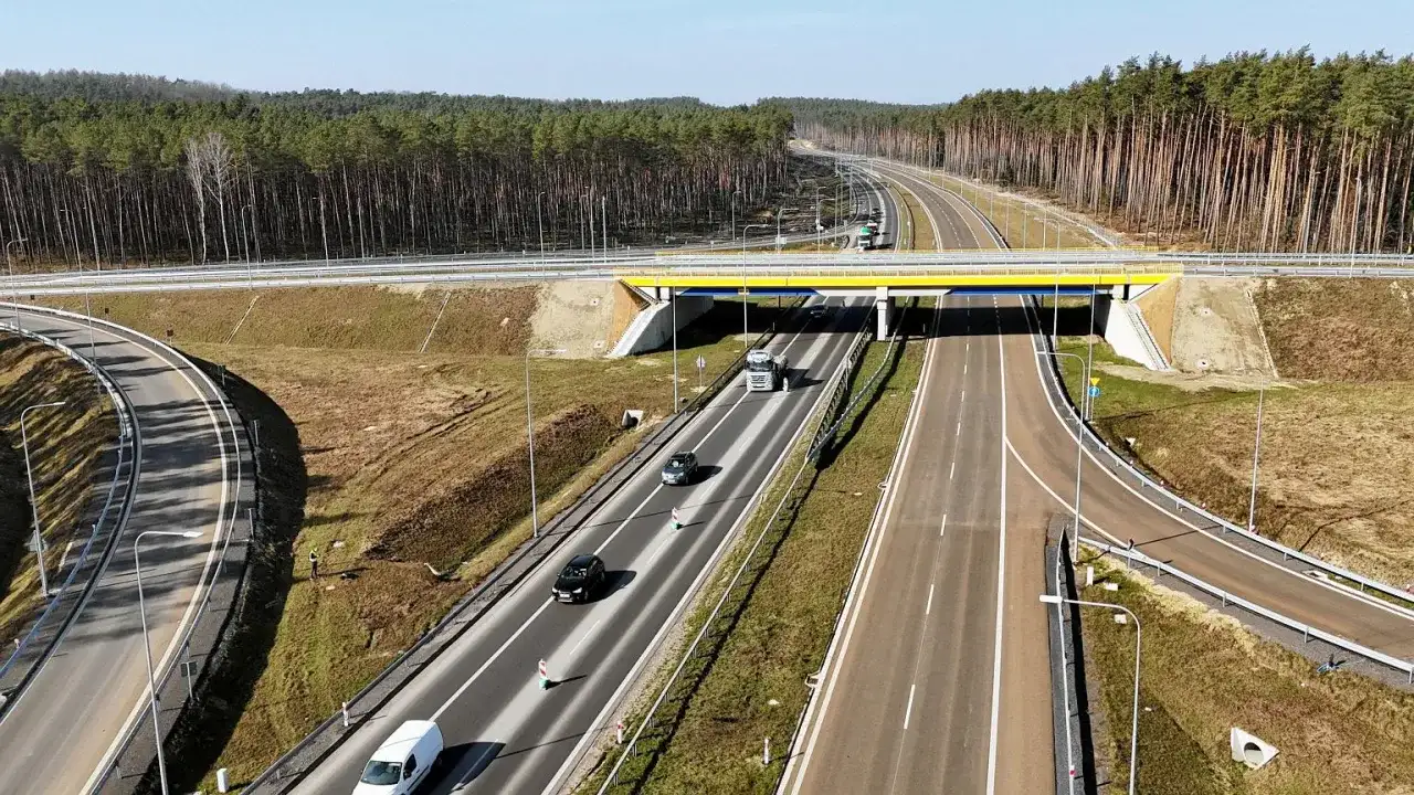 Widok z lotu ptaka na drogę ekspresową z mostem, samochodami i lasem w tle.