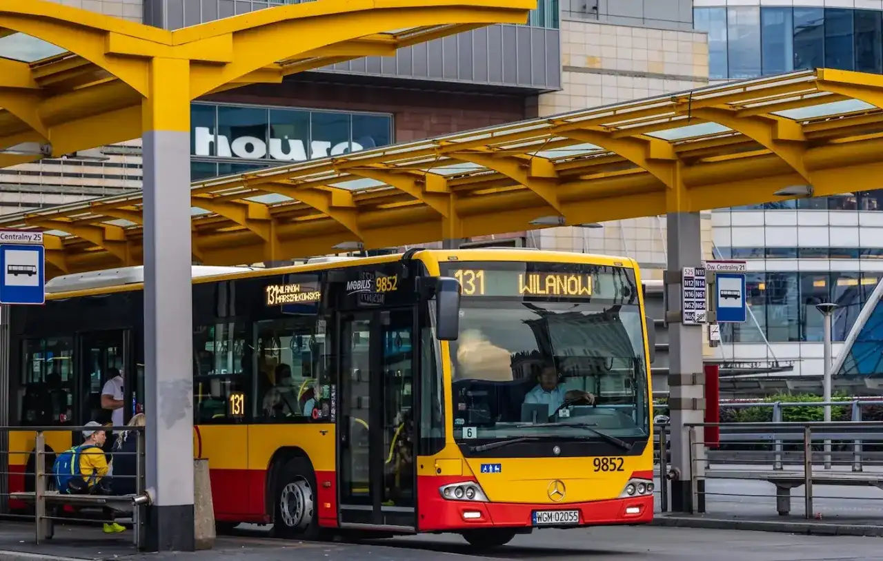 Żółto-czerwony autobus miejski na przystanku. Kierowca autobusu PKS, jak i jego zarobki, to temat dyskusji, ale ten pojazd wozi pasażerów.