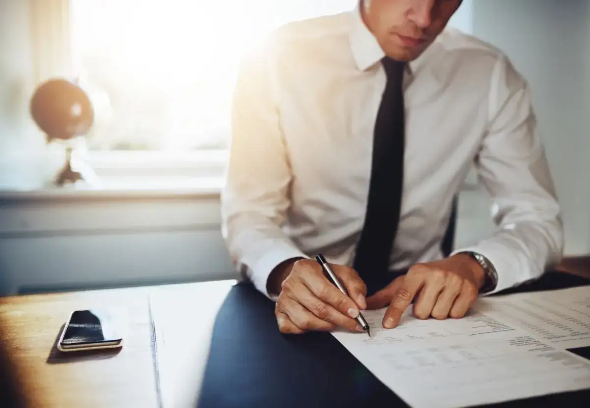 Mężczyzna w białej koszuli i czarnym krawacie podpisuje dokumenty, co może być krokiem do tego, jak zostać tłumaczem przysięgłym.