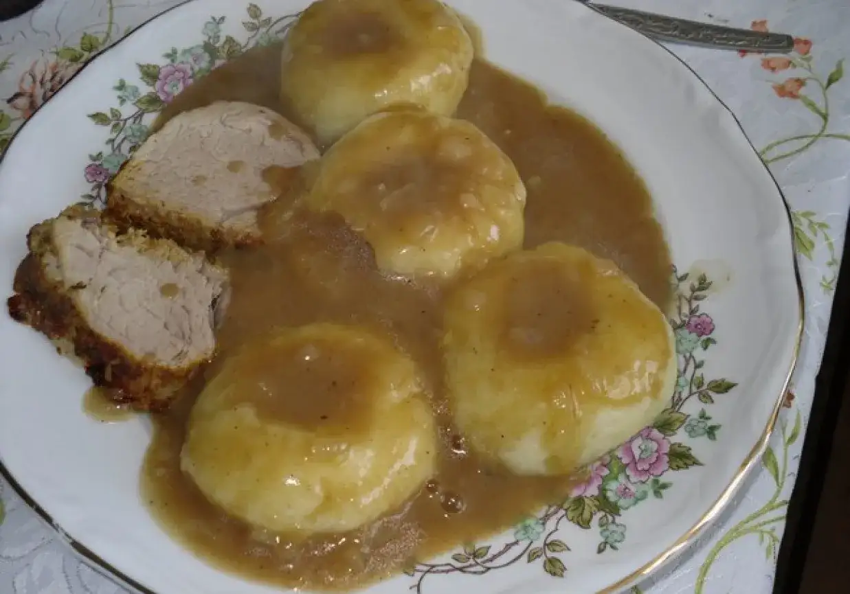 Kluseczki śląskie z mięsem i sosem na talerzu z kwiatowym wzorem.