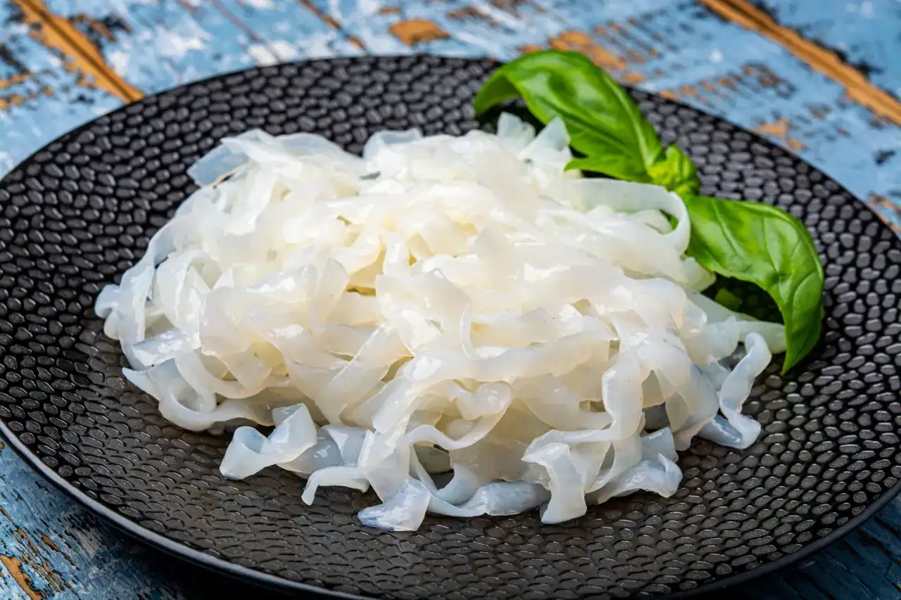 Makaron konjac na czarnym talerzu, z listkiem bazylii. To zdrowa alternatywa dla tradycyjnych klusek.
