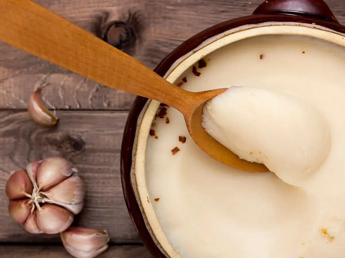 Gęsi smalec w glinianym naczyniu, drewniana łyżka ze smalcem, czosnek na drewnianym tle.