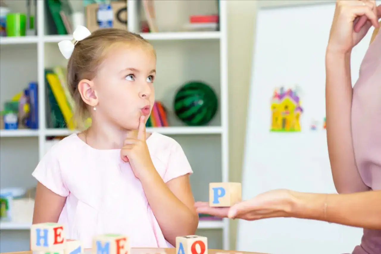 Dziewczynka z palcem przy ustach myśli podczas zabawy edukacyjnej z literkami.