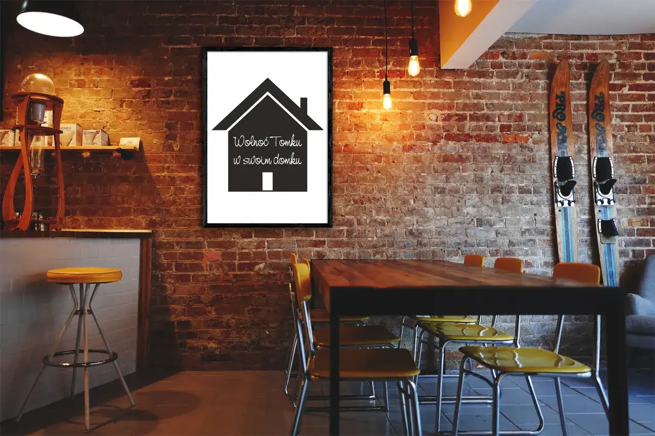 Obrazek z napisem "Wolnoć Tomku w swoim domku wiersz" na tle ceglanej ściany, obok nart i stołu z krzesłami.