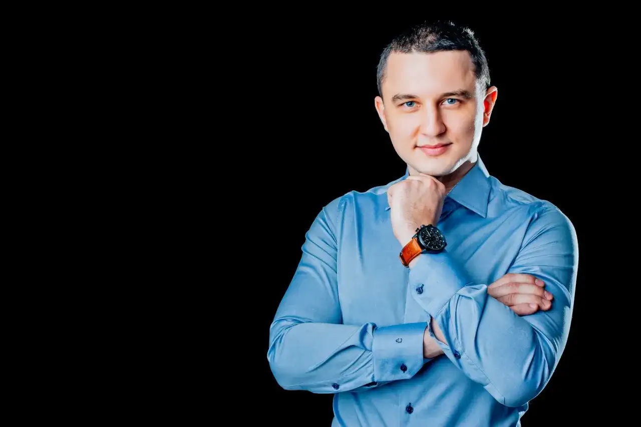 Mężczyzna w niebieskiej koszuli, z rękami skrzyżowanymi na piersi, podczas sesji biznesowej.