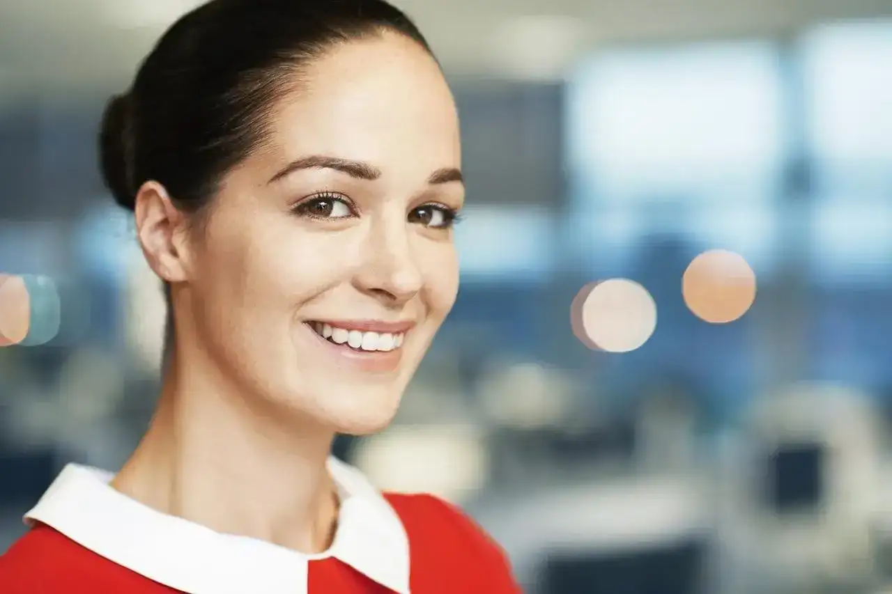 Uśmiechnięta kobieta w czerwonej sukience z białym kołnierzykiem, z włosami upiętymi w kok.