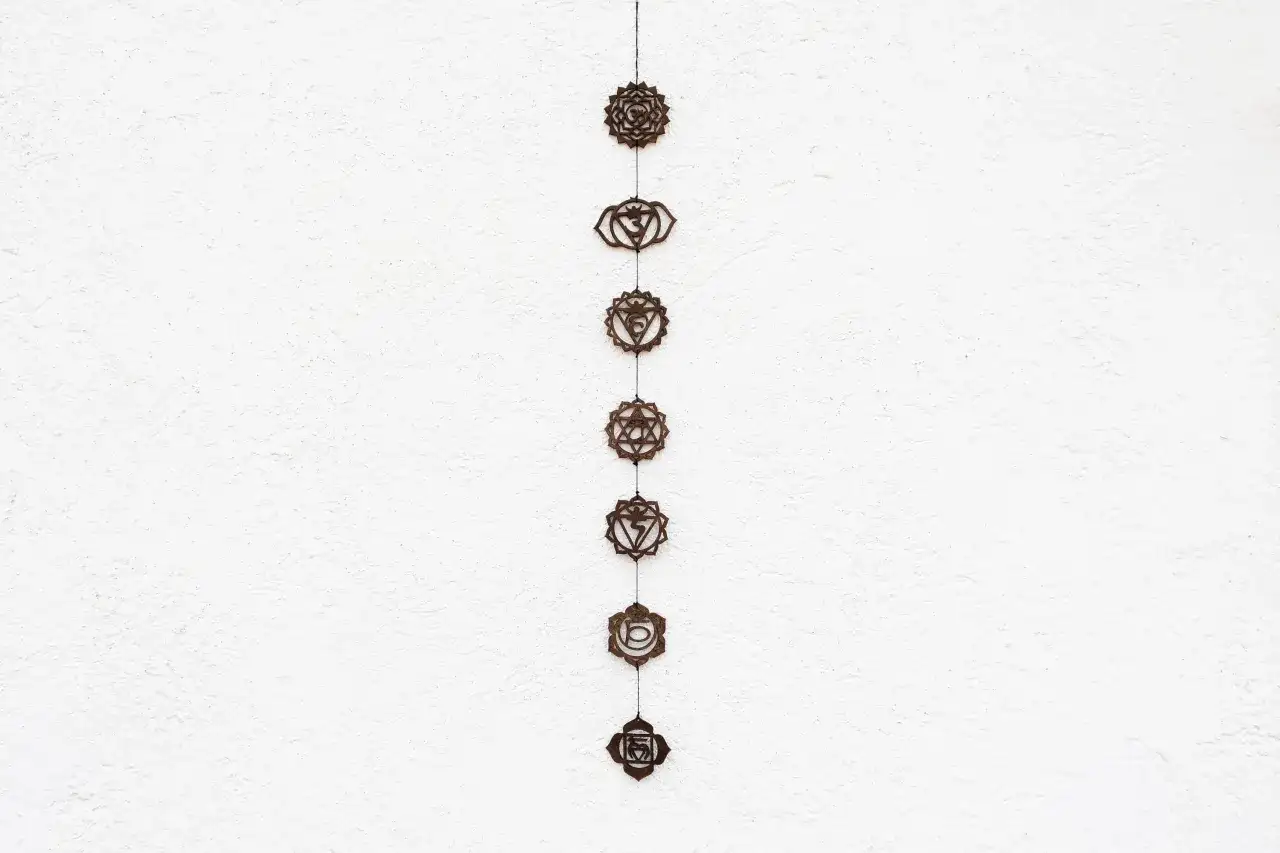 Wisząca ozdoba z siedmioma symbolami czakr na białej, teksturowanej ścianie.