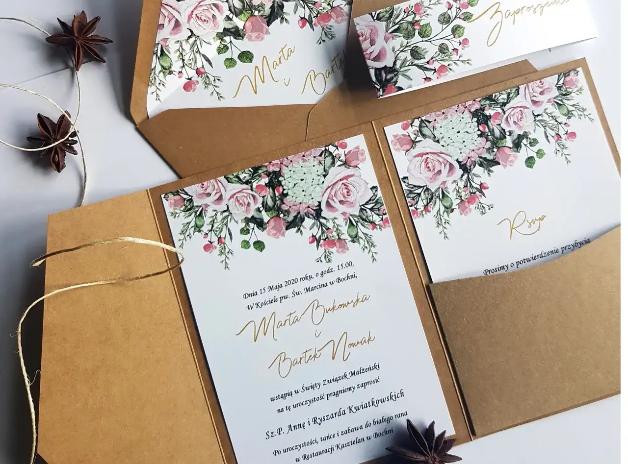 Eleganckie zaproszenia ślubne z motywem róż i zieleni, w brązowych kopertach.