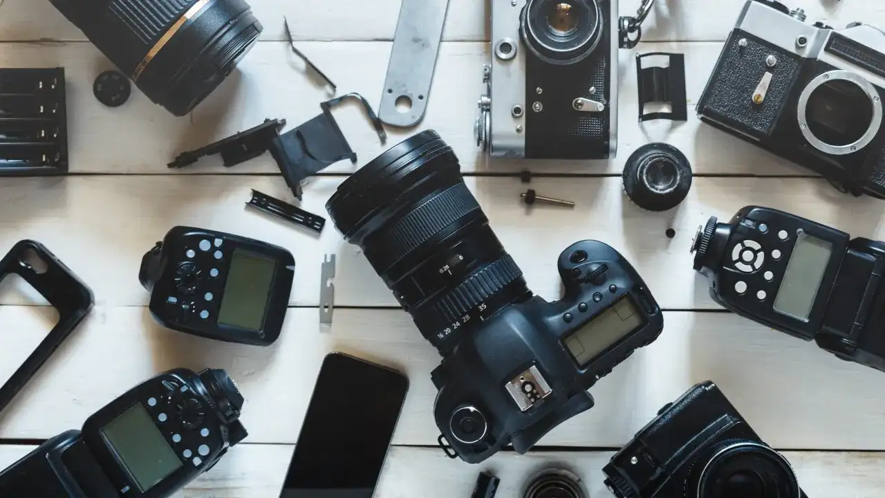 Rozłożone na białym tle aparaty fotograficzne, obiektywy i lampy błyskowe.