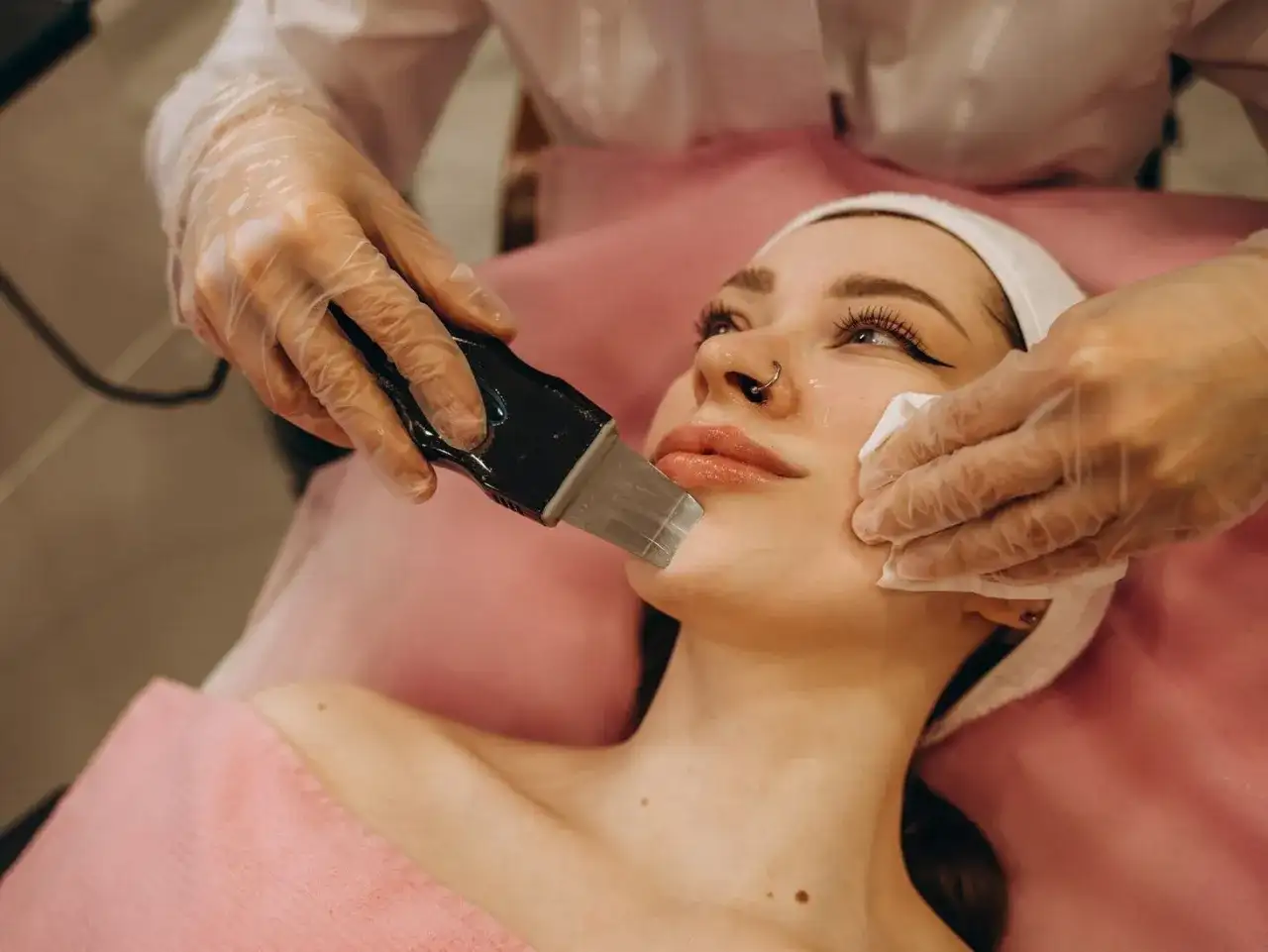 Zabieg peelingu kawitacyjnego. Kosmetyczka w rękawiczkach używa urządzenia do oczyszczania twarzy. Jakie kosmetyki do peelingu kawitacyjnego?