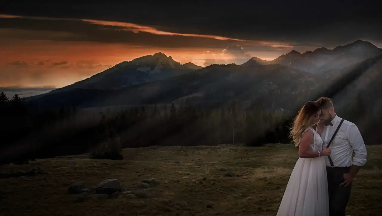 Para przytula się na tle górskiego krajobrazu o zachodzie słońca. Idealny przykład, jak pozować do zdjęć w parze.