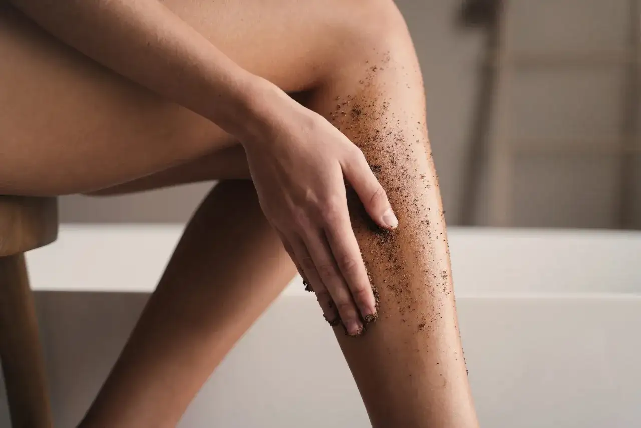 Dłoń rozprowadza kawowy peeling na skórze nogi, dbając o gładkość i redukcję cellulitu.