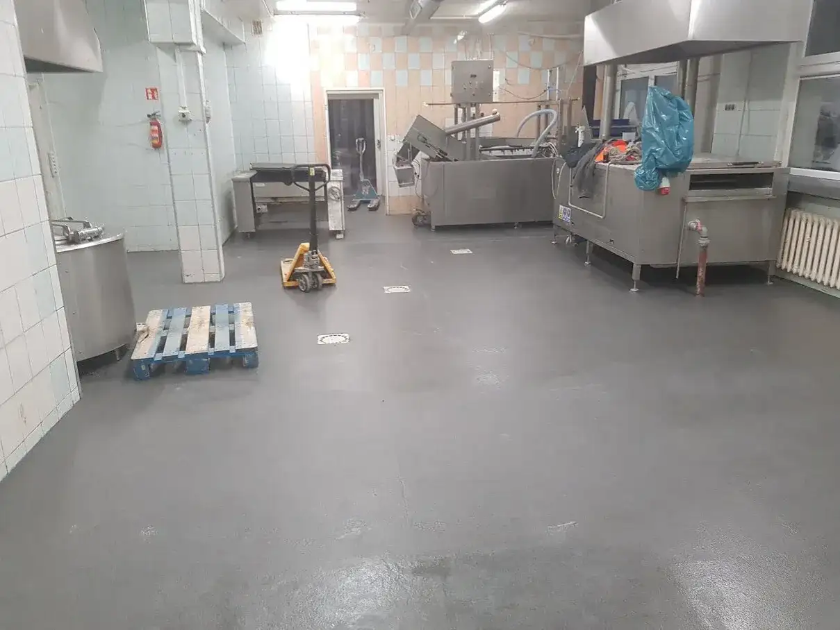 Nowa, szara wylewka betonowa w kuchni przemysłowej schnie, czekając na dalsze prace.