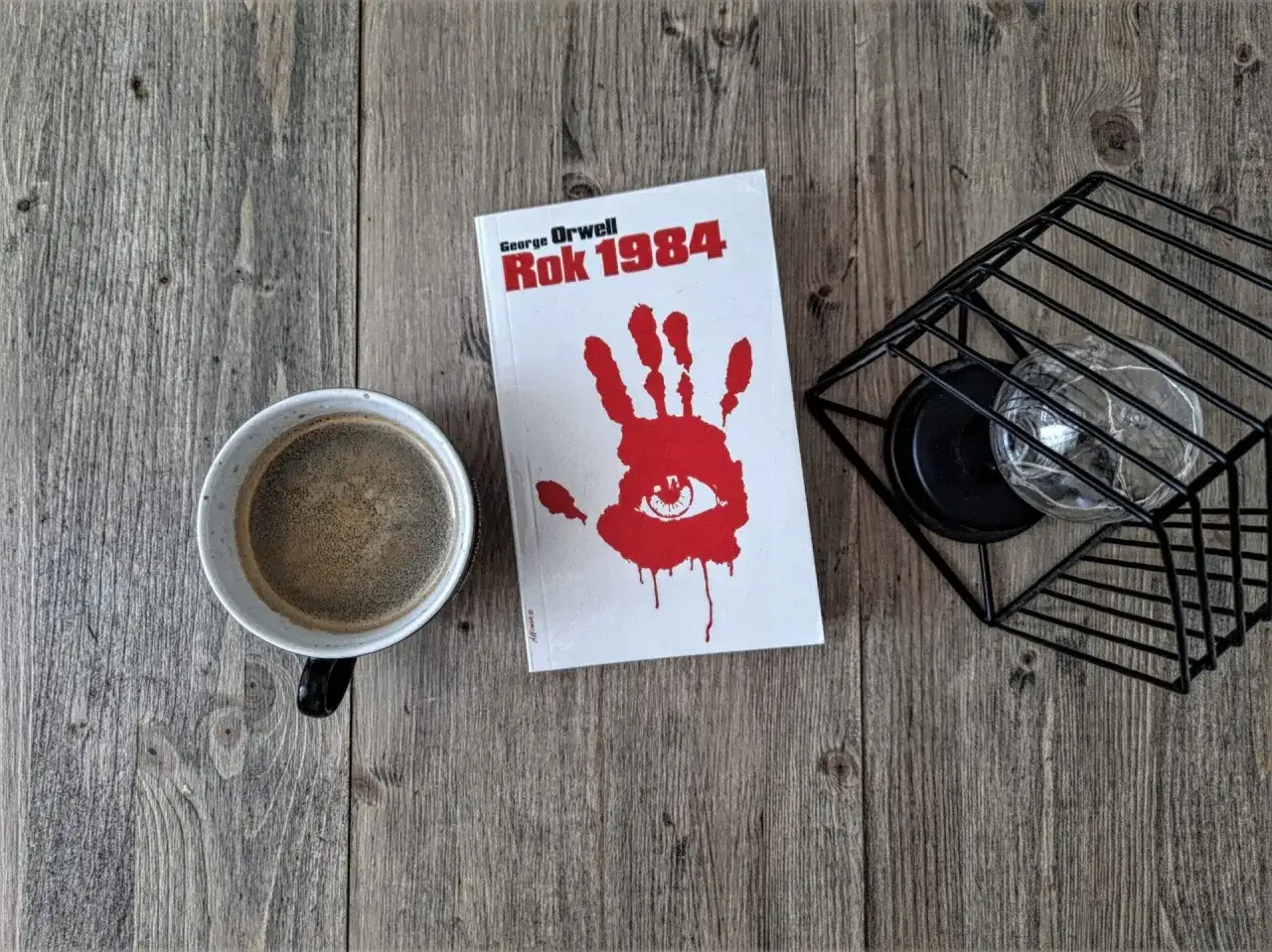Kawa i książka "Rok 1984" George'a Orwella na drewnianym stole. Recenzja tej ponadczasowej lektury czeka.