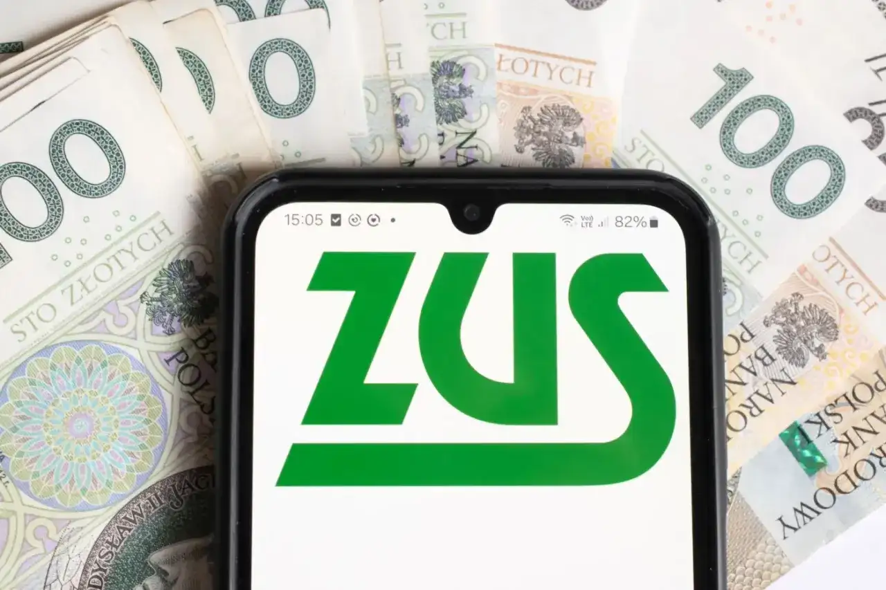 ZUS na ekranie telefonu, otoczony banknotami 100 zł. Symbolizuje to świadczenia, np. dodatek do emerytury dla 1 grupy inwalidzkiej.