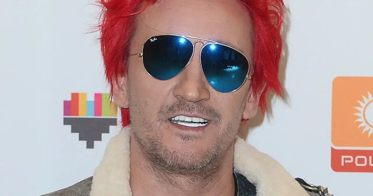 Michał Wiśniewski w okularach przeciwsłonecznych i z czerwonymi włosami. Choć nie widać całego ciała, jego postawa sugeruje, że ile wzrostu ma Michał Wiśniewski, nie jest kluczowe dla jego charyzmy.