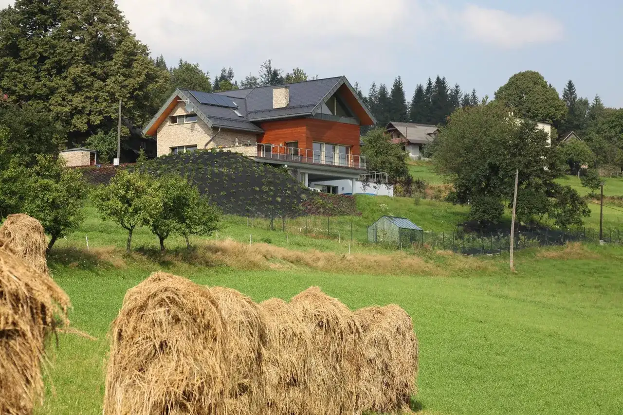 Nowoczesna zabudowa zagrodowa, kto może budować? Dom z panelami słonecznymi i drewnianą elewacją na wzgórzu, obok stogi siana.