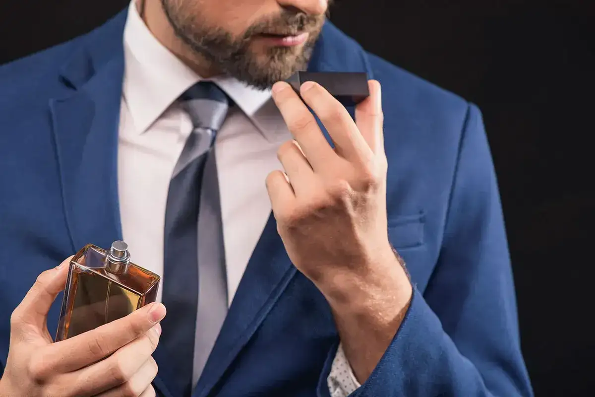 Mężczyzna w garniturze wącha perfumy z buteleczki.