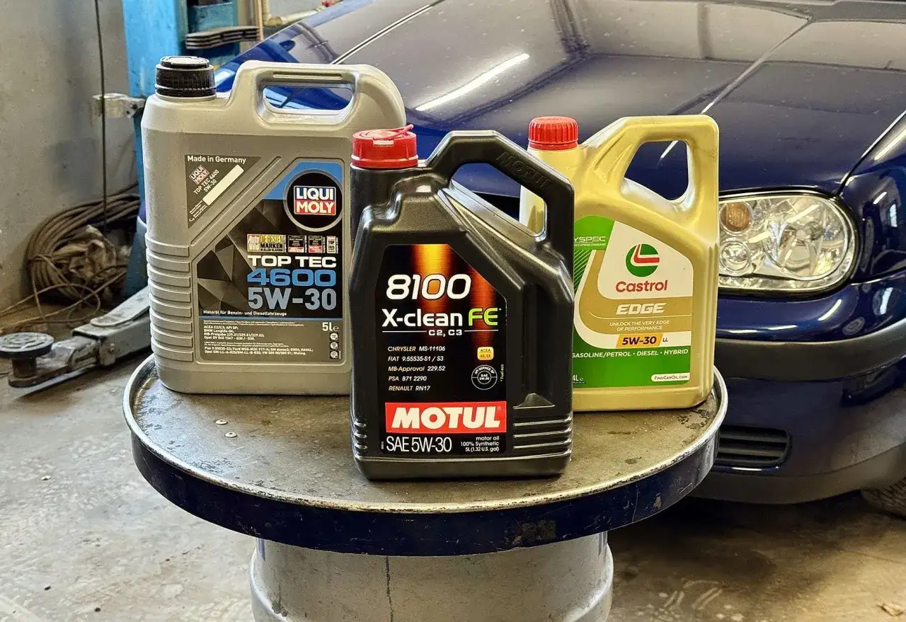 Trzy kanistry z olejem silnikowym: Liqui Moly, Motul i Castrol, na tle niebieskiego samochodu.