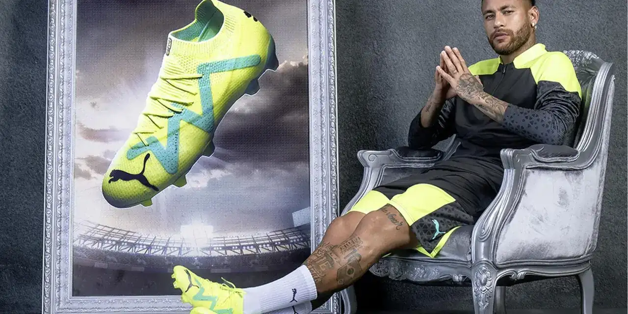 Neymar w neonowych butach piłkarskich na tle stadionu. Buty z technologią Phat Tape idealne na nawierzchnię turf.