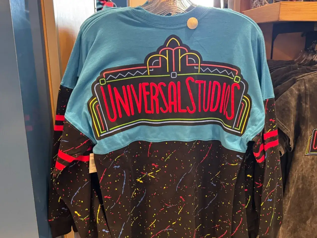 Turkusowy longsleeve z neonowym napisem "Universal Studios" i kolorowymi plamkami na czarnym tle. Idealny na wycieczkę do parku rozrywki!
