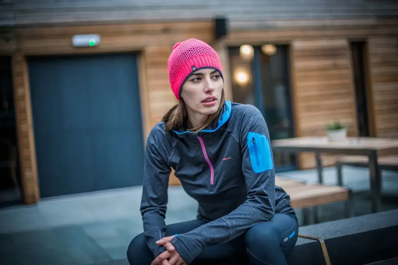 Kobieta w różowej czapce i sportowej bluzie siedzi na zewnątrz.