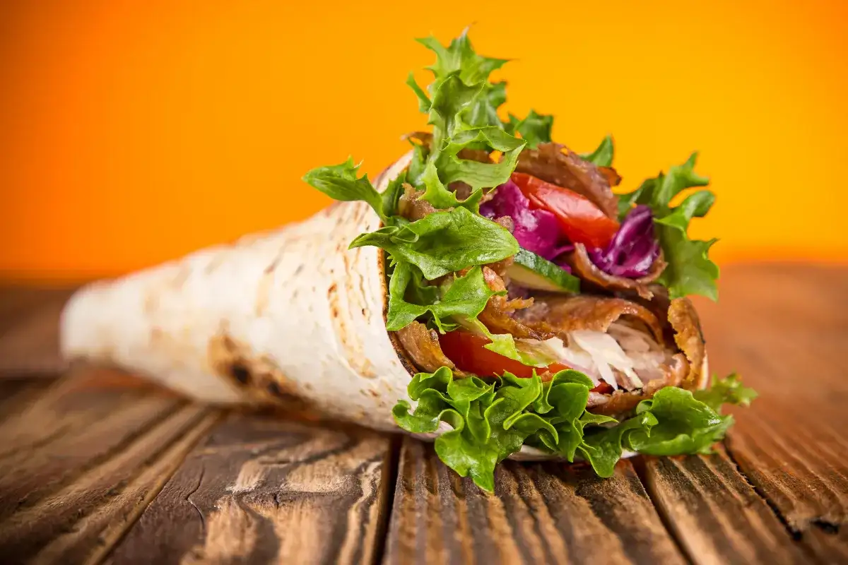 Kebab zawinięty w placek z mięsem, warzywami i sałatą na drewnianym stole.