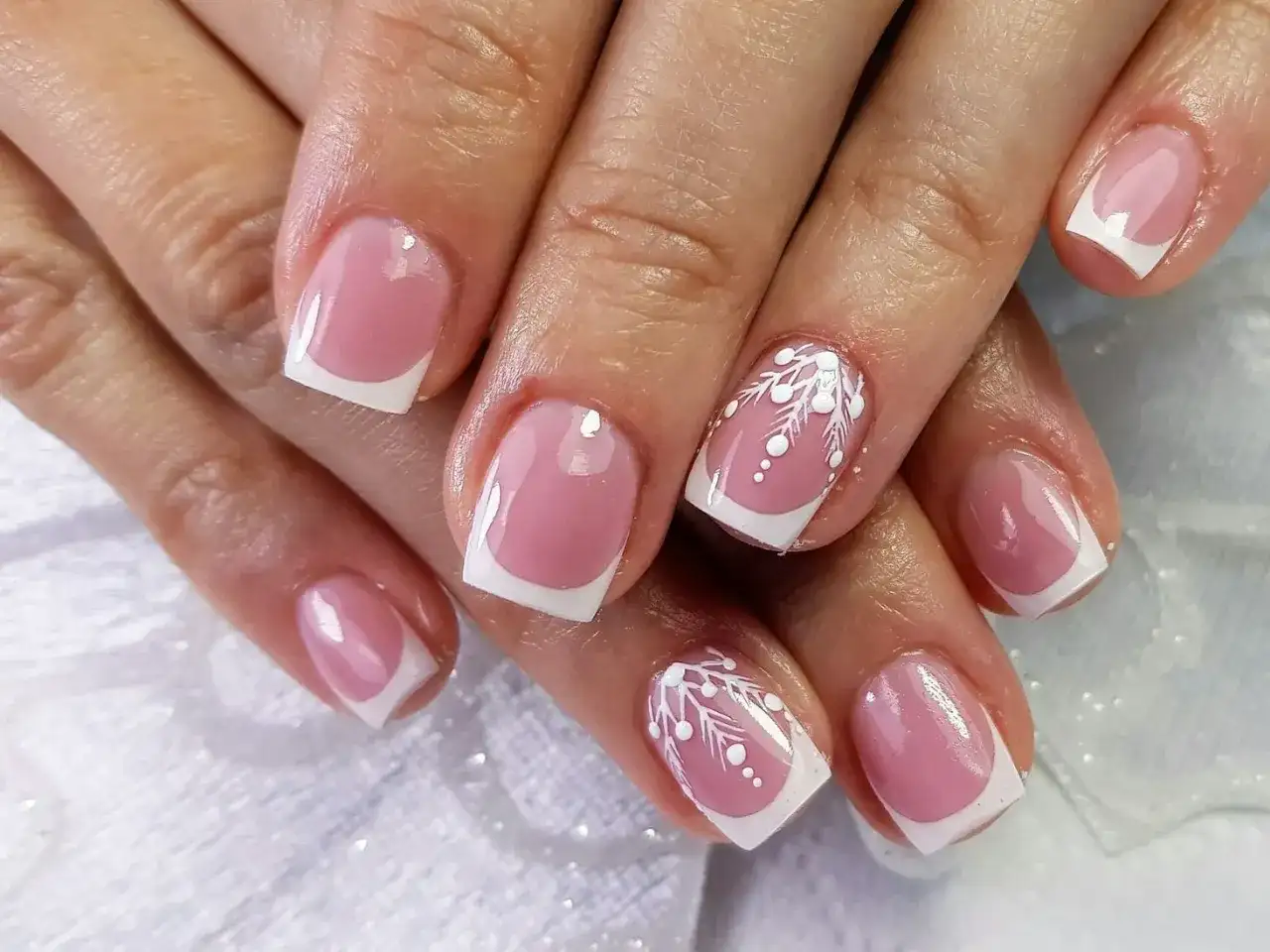 Dłonie z paznokciami żelowymi w stylu francuskim, zdobione białymi wzorami.
