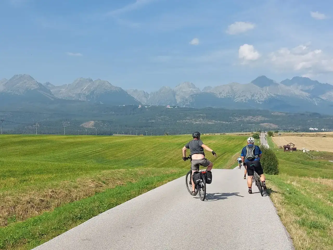 Rowerzyści przemierzają malowniczą trasę. W tle rozciągają się majestatyczne Tatry, tworząc piękny historyczno kulturowo przyrodniczy szlak wokół gór.